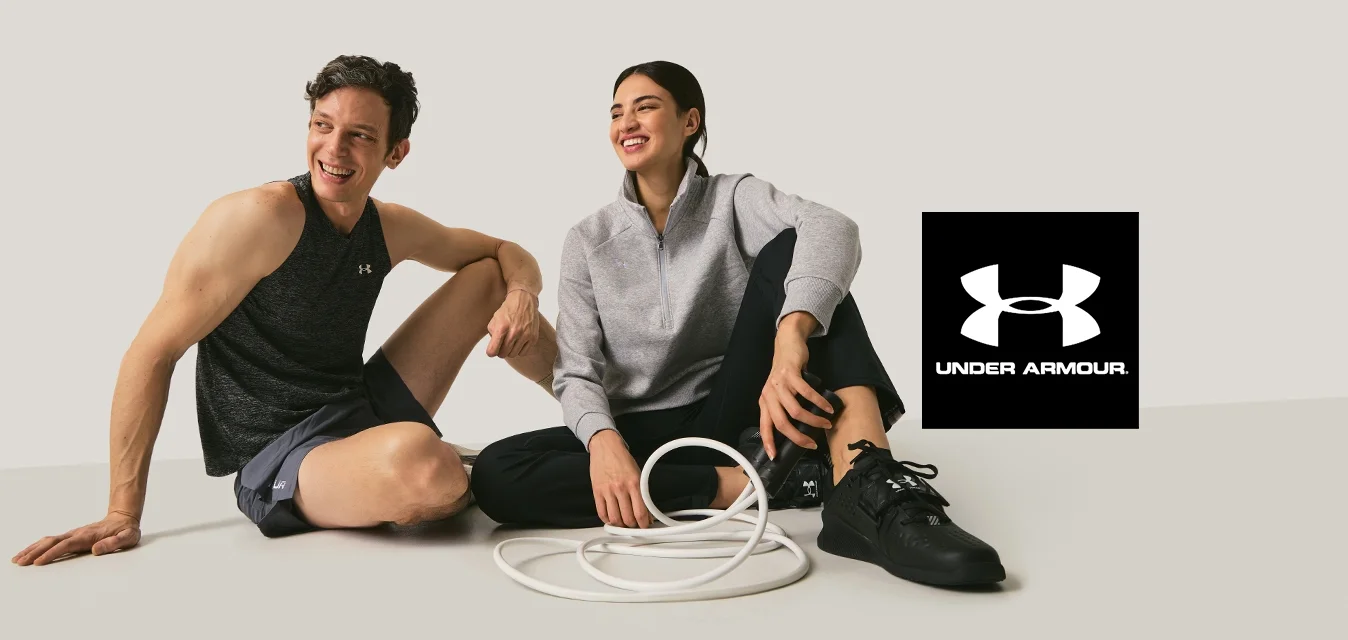 Dos adultos con ropa deportiva sentados en el suelo sonriendo, con una cuerda de ejercicio blanca enrollada entre ellos sobre un fondo liso.