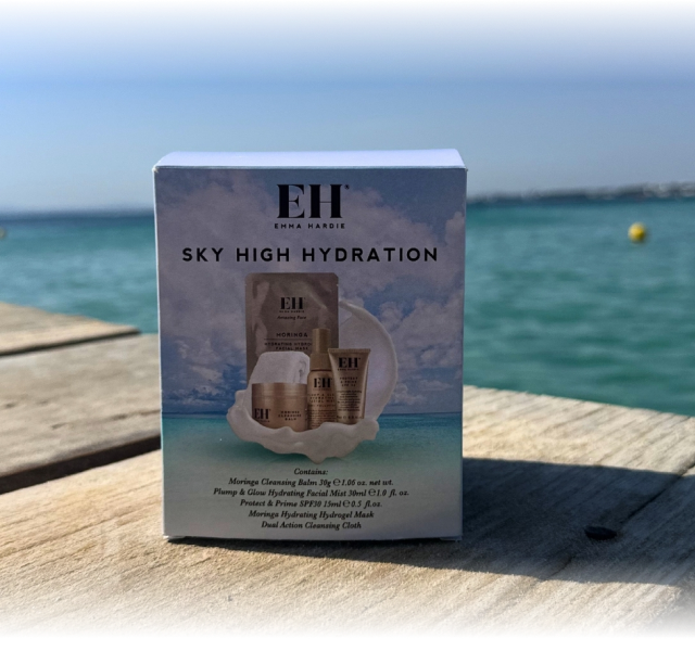 Emma Hardie Sky High Hydration travel skincare set beside the sea on a sunny wooden deck.