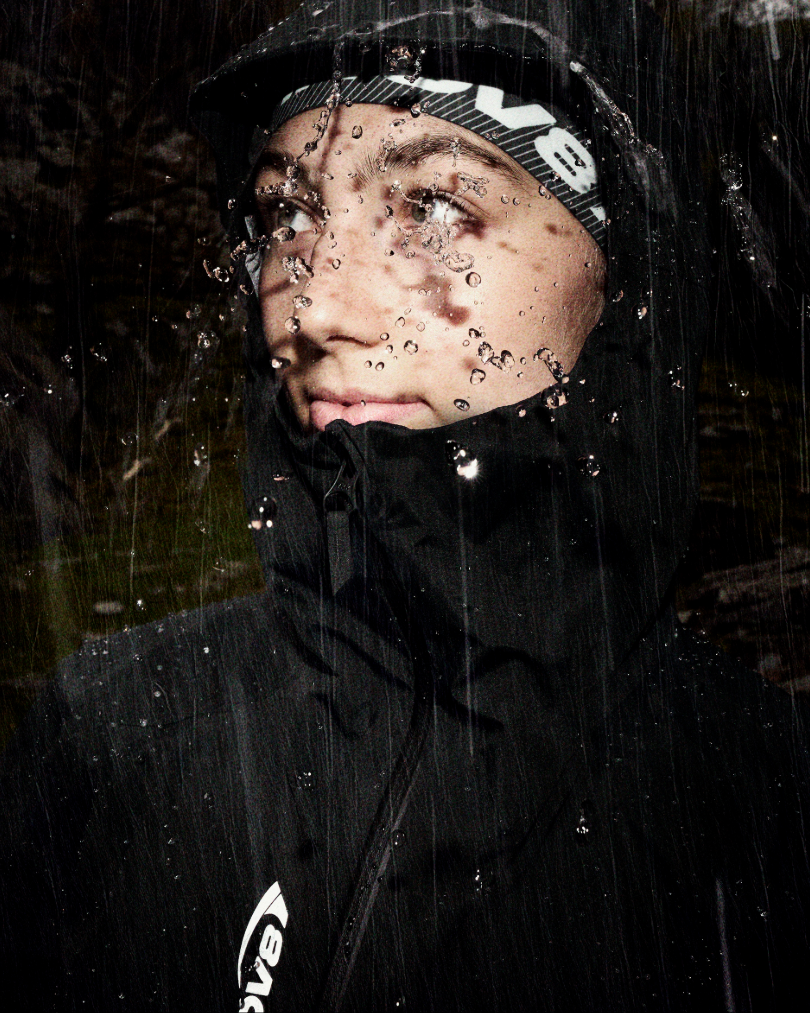 An athlete wearing a waterproof jacket with rain splashing off the hood