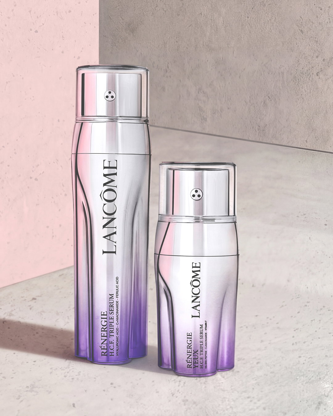 Flaconi metallici Lancôme Rénergie H.C.F. Triple Serum e Rénergie Yeux con sfumature viola su fondo rosa e grigio