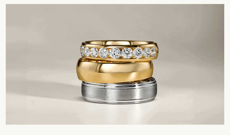 Three stacked ring bands of various metals: gold with diamonds, polished gold & silver.