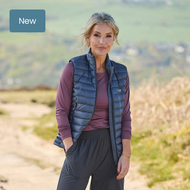Rab new-season outdoor outfit featuring a navy insulated gilet and long-sleeve top, photographed on a countryside trail.
