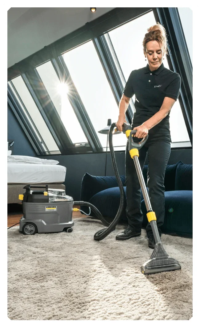 Woman in a living space wearing a black polo shirt and cleaning a cream carpet using the Kärcher Pro Puzzi 800 Carpet Cleaner