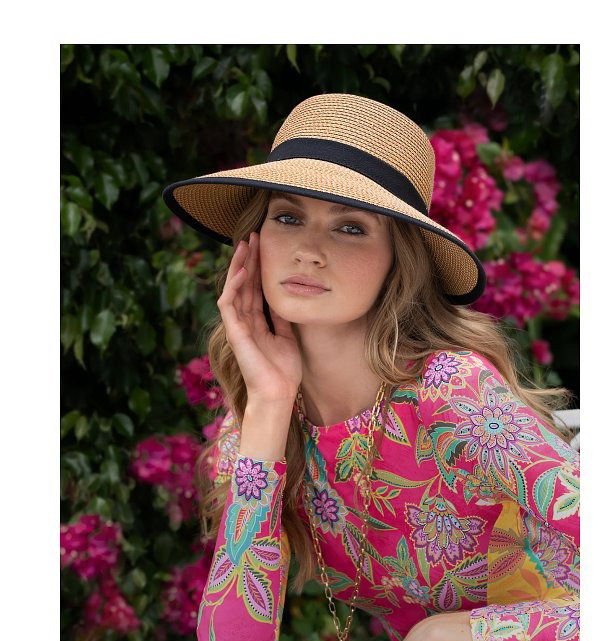 A woman in a colorful floral dress wearing a straw hat, and another woman in a white hat.