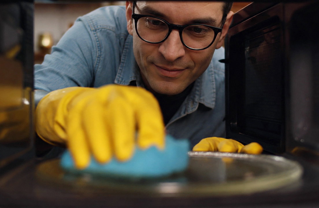 A man wearing yellow gloves cleans the inside of a microwave
