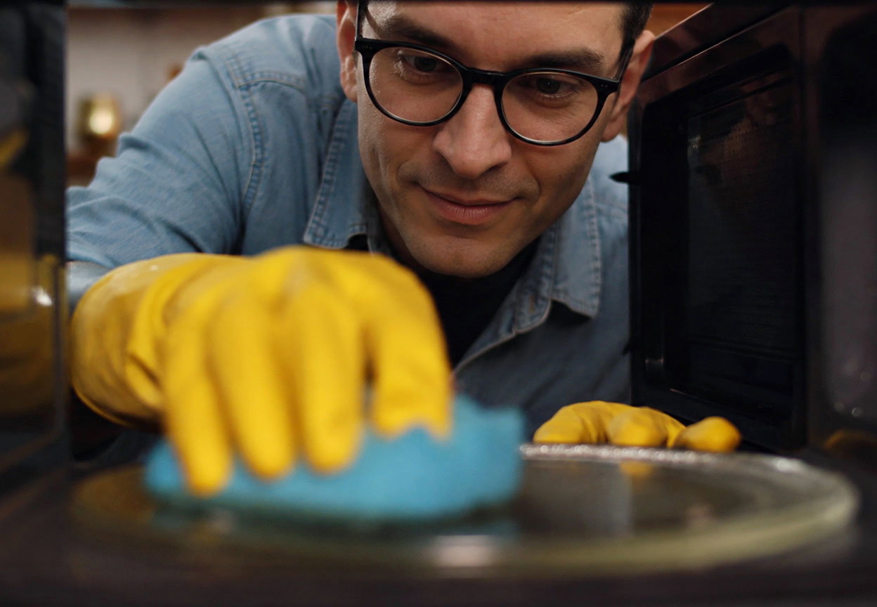 A man wearing yellow gloves cleans the inside of a microwave