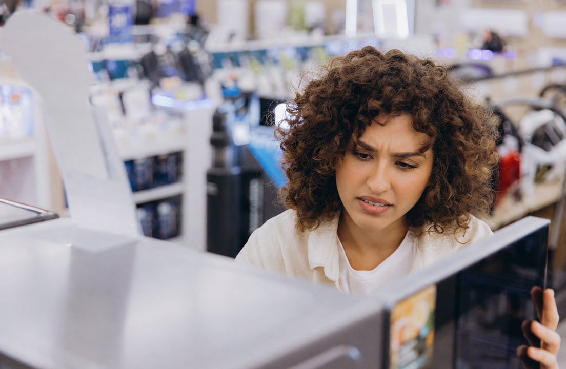 A woman examines an open microwave while shopping for a new appliance