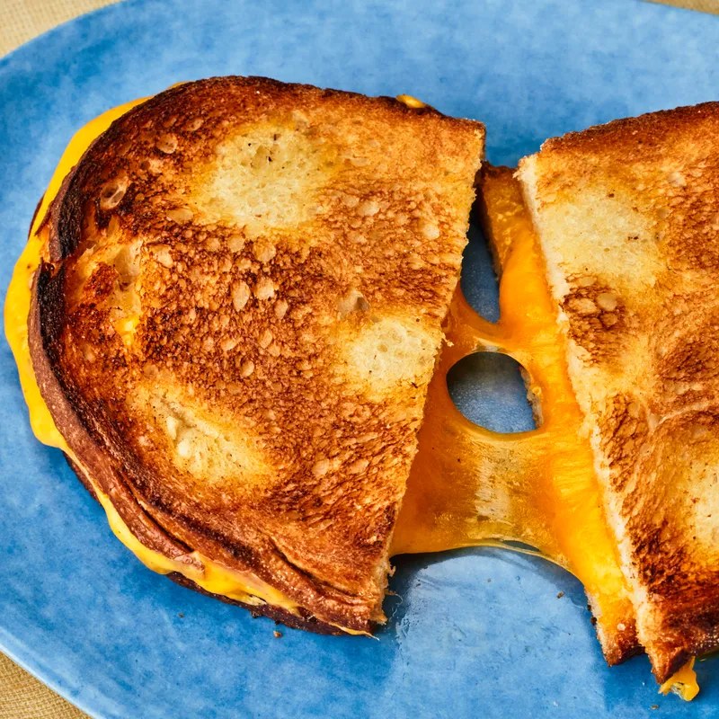 A halved grilled cheese sandwich with speckles on the toasted side of the bread.