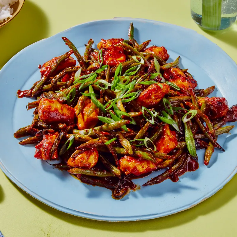 Gochujang Chicken and Scallion Stir Fry on a blue plate and on a green background