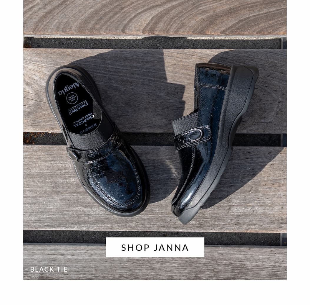 An overhead view of a pair of glossy, black patent leather Alegria Janna shoes arranged on gray wooden planks. One shoe shows the interior insole detailing charcoal and bamboo technology. A button reads 'SHOP JANNA'.