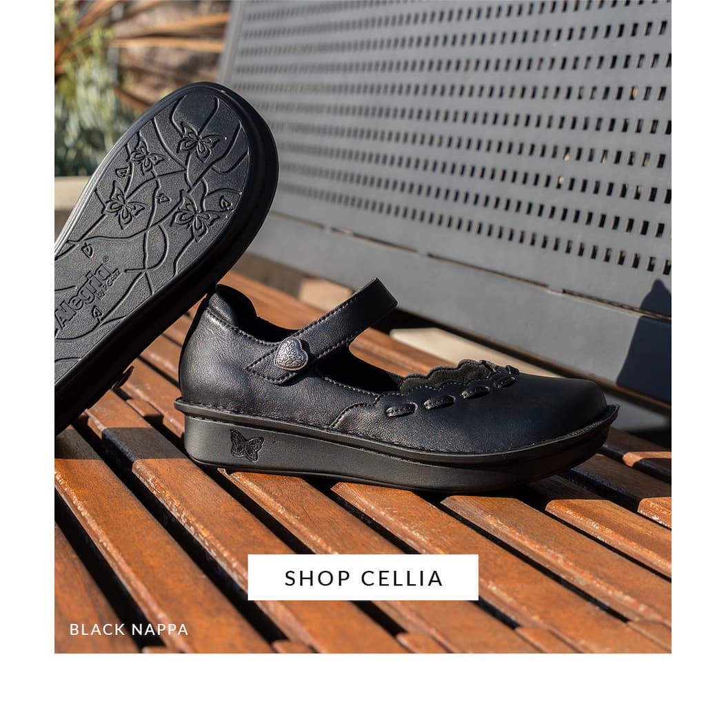 A black nappa leather Alegria Cellia Mary Jane shoe sits on a wooden slatted bench next to another shoe flipped to display its decorative patterned outsole. A button reads 'SHOP CELLIA'..