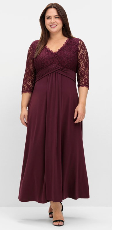 Ein Model trägt ein burgund farbenes Abendkleid mit floraler Spitze, V-Ausschnitt und dekorativem Zier-Knotendetail in der Taille
