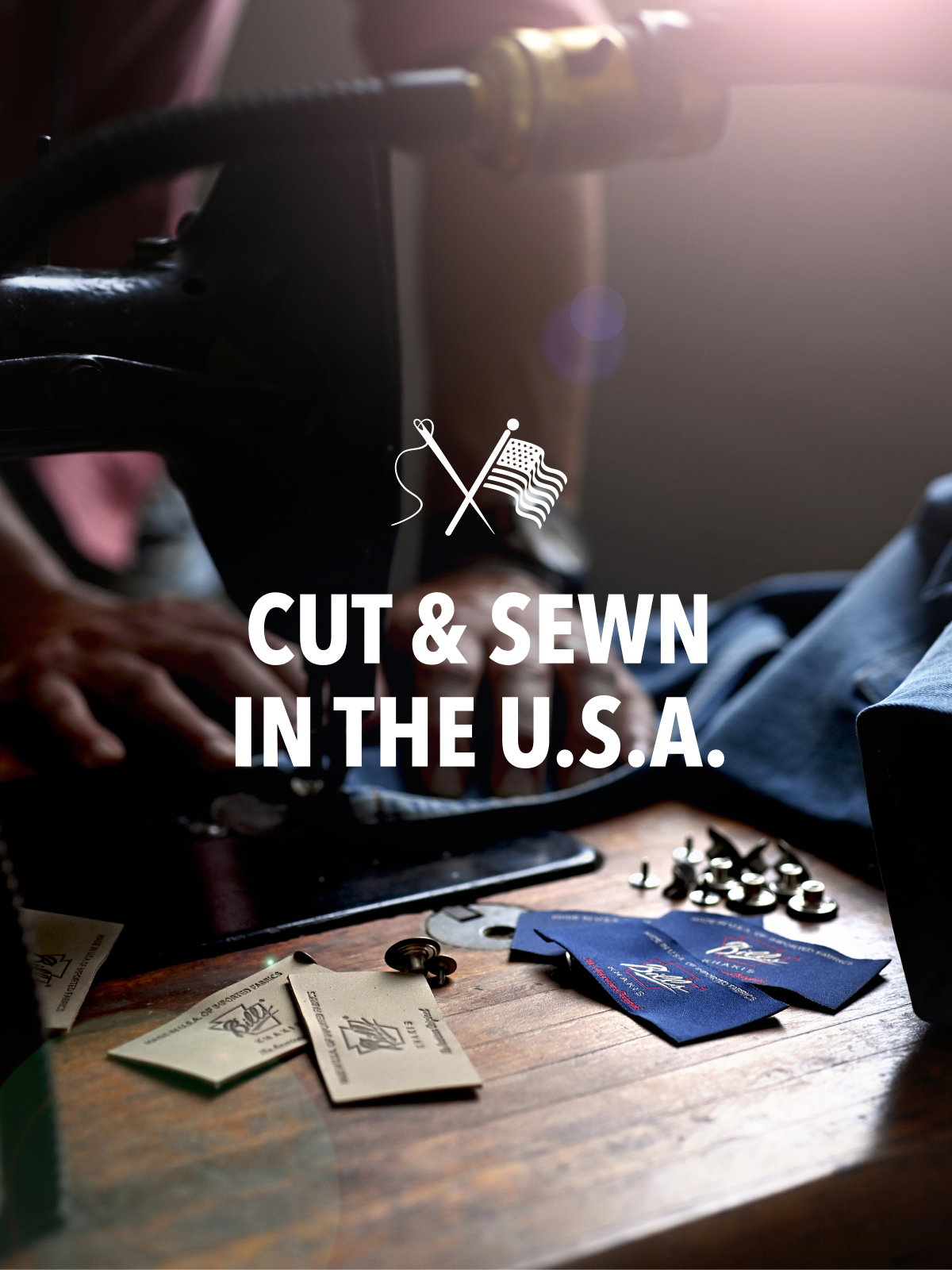 Hands work on a vintage sewing maching dewing Bills Khakis fabric tags with a dramatic lighting. Text reads Cut and Sewn in the USA with a needle and flag icon