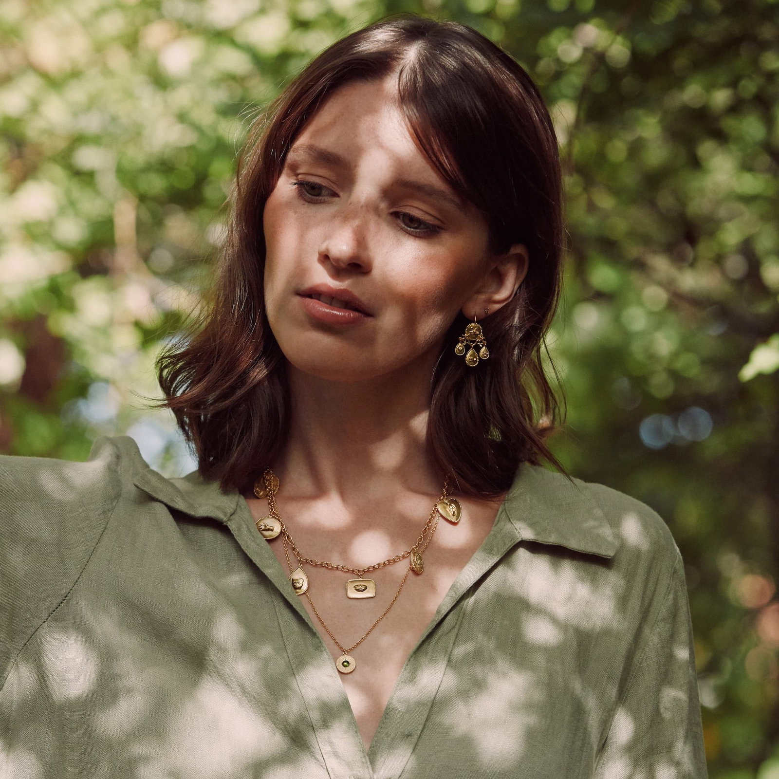 Model wearing layered gold jewellery from the Alex Monroe Summer Favourites collection, against a summer lit forest background.