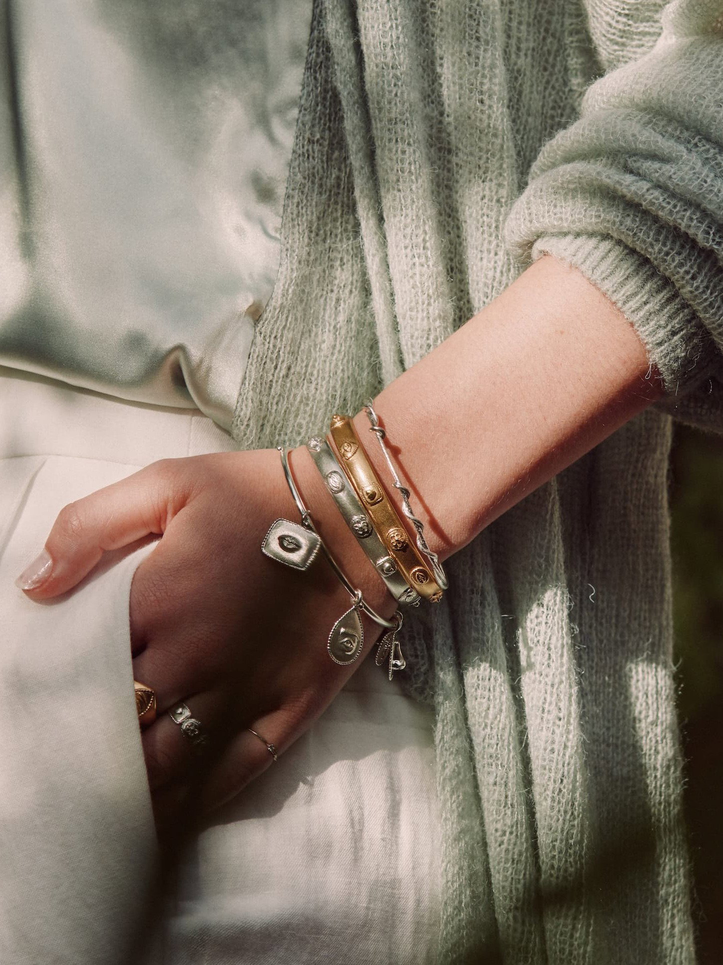 Close-up of stacked gold and gemstone bracelets worn with a green linen dress.