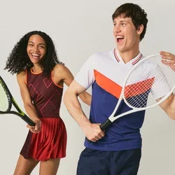 Un homme et une femme souriants en tenue de tennis posent avec des raquettes, debout devant un fond clair uni.