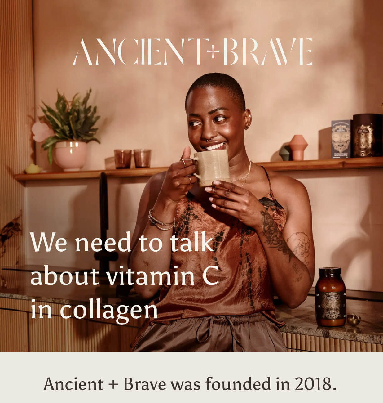 Ancient + Brave. A woman smiling and holding a ceramic mug, with a jar of True Collagen on the counter beside her. We need to talk about vitamin C in collagen.