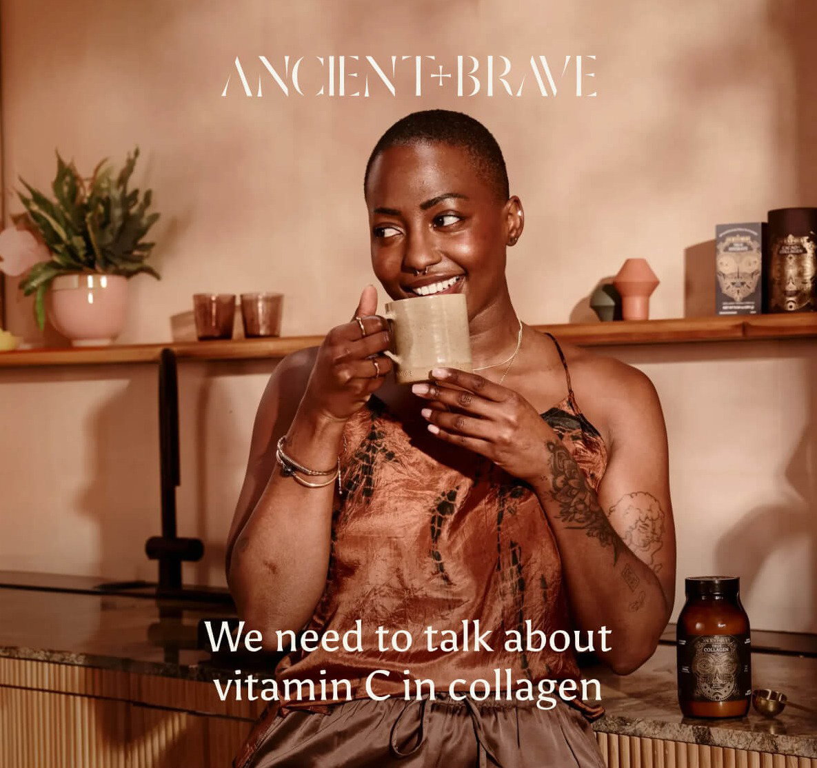 Ancient + Brave. A woman smiling and holding a ceramic mug, with a jar of True Collagen on the counter beside her. We need to talk about vitamin C in collagen.