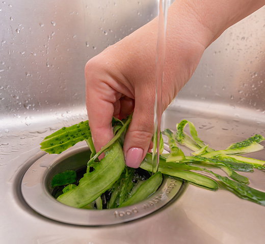 A hand putting food waste down a garbage disposal