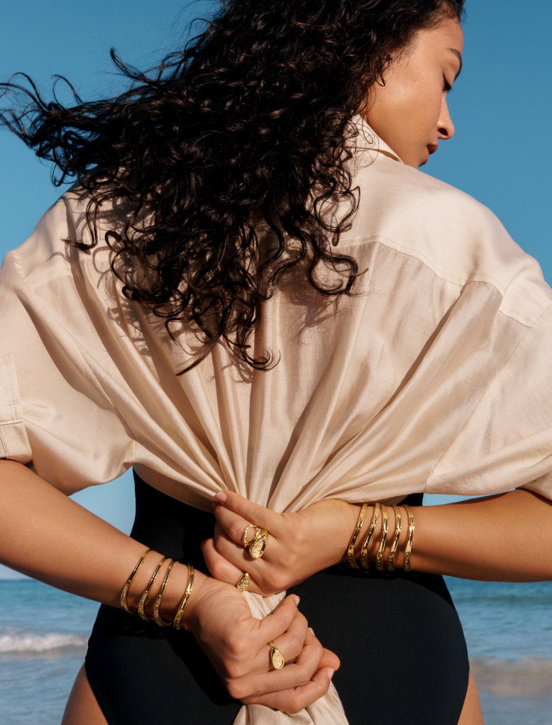 A model scrunches a blouse and wears 14k gold-plated jewellery.