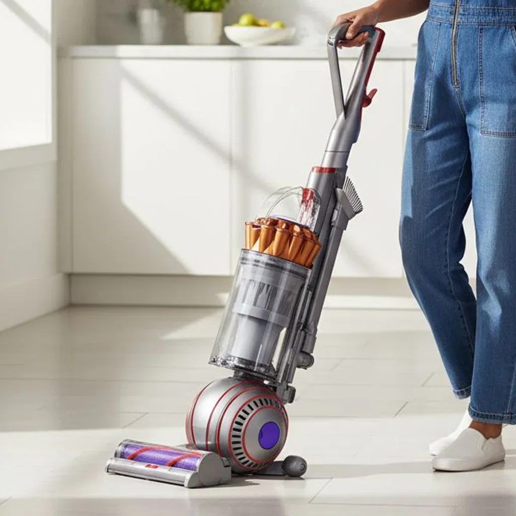 Person holding a Dyson upright vacuum cleaner with purple accent wheels on a clean kitchen floor.