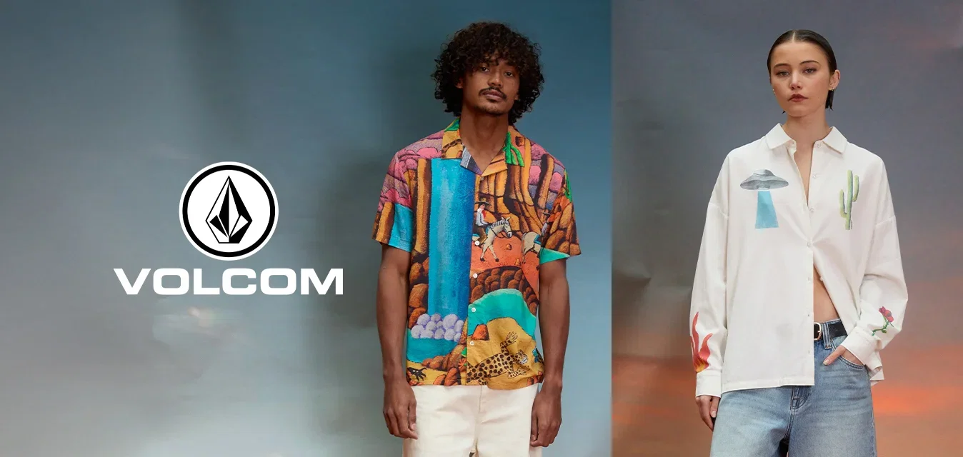 Hombre con camisa de manga corta con estampado colorido y pantalones cortos blancos está junto a mujer con camisa blanca con diseños de ovnis y cactus y pantalones cortos de mezclilla.