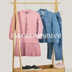 Perchero de madera con un vestido de punto rosa y un cárdigan, una camisa azul con estampado y unos vaqueros, zapatillas negras y rosas encima y debajo del perchero.
