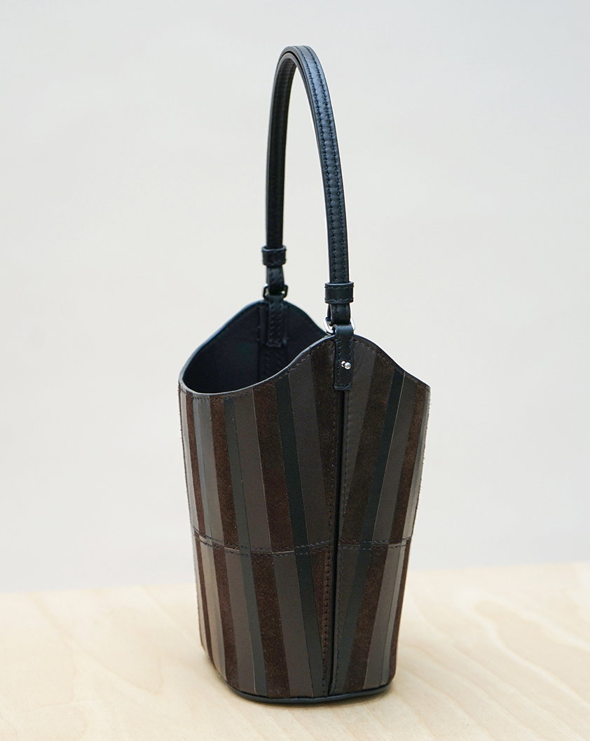 Still Life Image of Mini Bucket Bag in Intarsia in Black/Espresso on a Wooden Plinth.