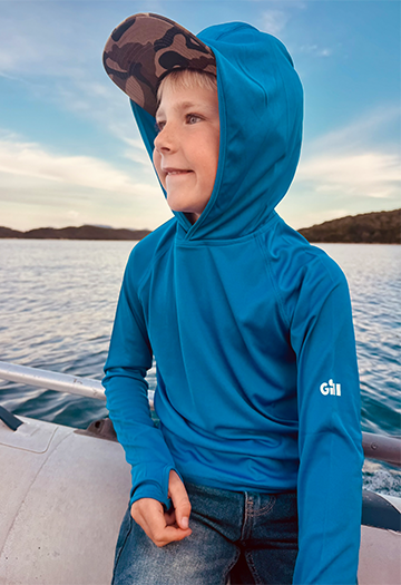 Junior on the side of a boat wearing Tidal Blue UV Tec Hoody