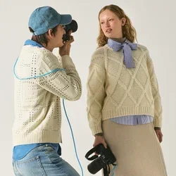 Fotograaf met pet en trui maakt foto van vrouw in gebreide trui en beige rok die zwarte laarzen vasthoudt tegen effen achtergrond.