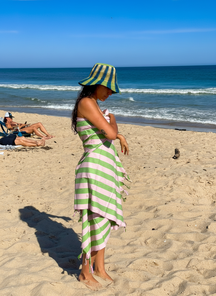 Woman in striped hat and towel on a beach with ocean in background.