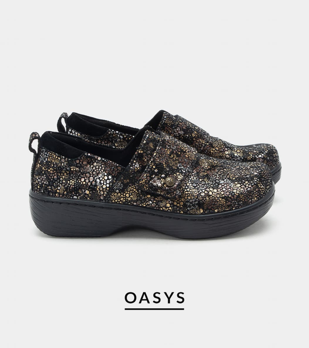 A side profile view of a pair of "Oasys" closed-toe slip-on shoes. The shoes feature a textured metallic gold, silver, and black mosaic pattern across the upper, an adjustable hook-and-loop strap with a decorative button, and a thick, supportive black rocker sole.