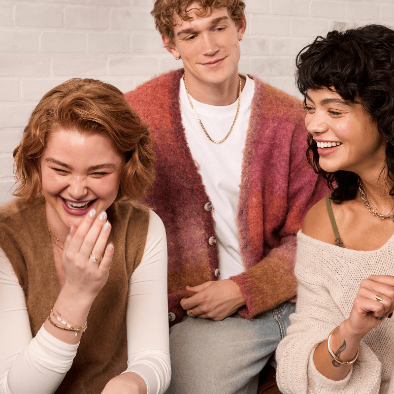 Three friends laughing together. Each one is wearing fashion jewellery; chains, bracelets, rings and earrings.