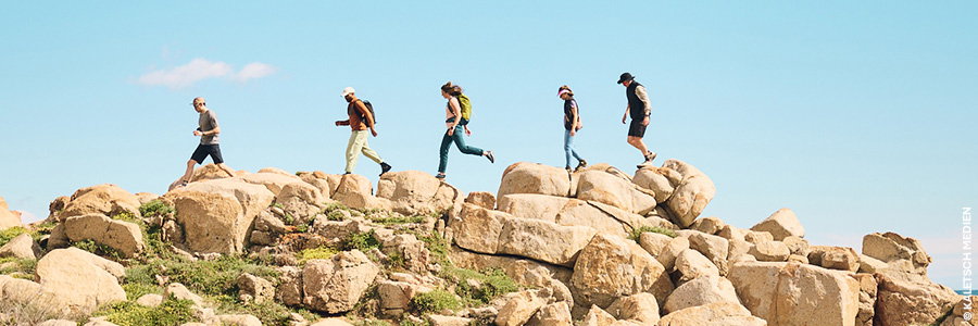 Five hikers crossing a field of sandstone boulders