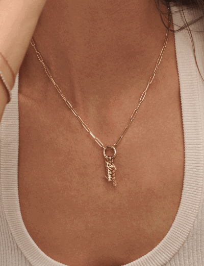 Close-up of a woman wearing a yellow gold name pendant necklace on a fine chain.