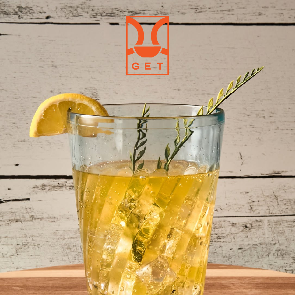 GET Tahiti™ tumbler filled with a sparkling beverage over ice, garnished with a lemon wedge and herb sprigs, displayed on a wood surface.