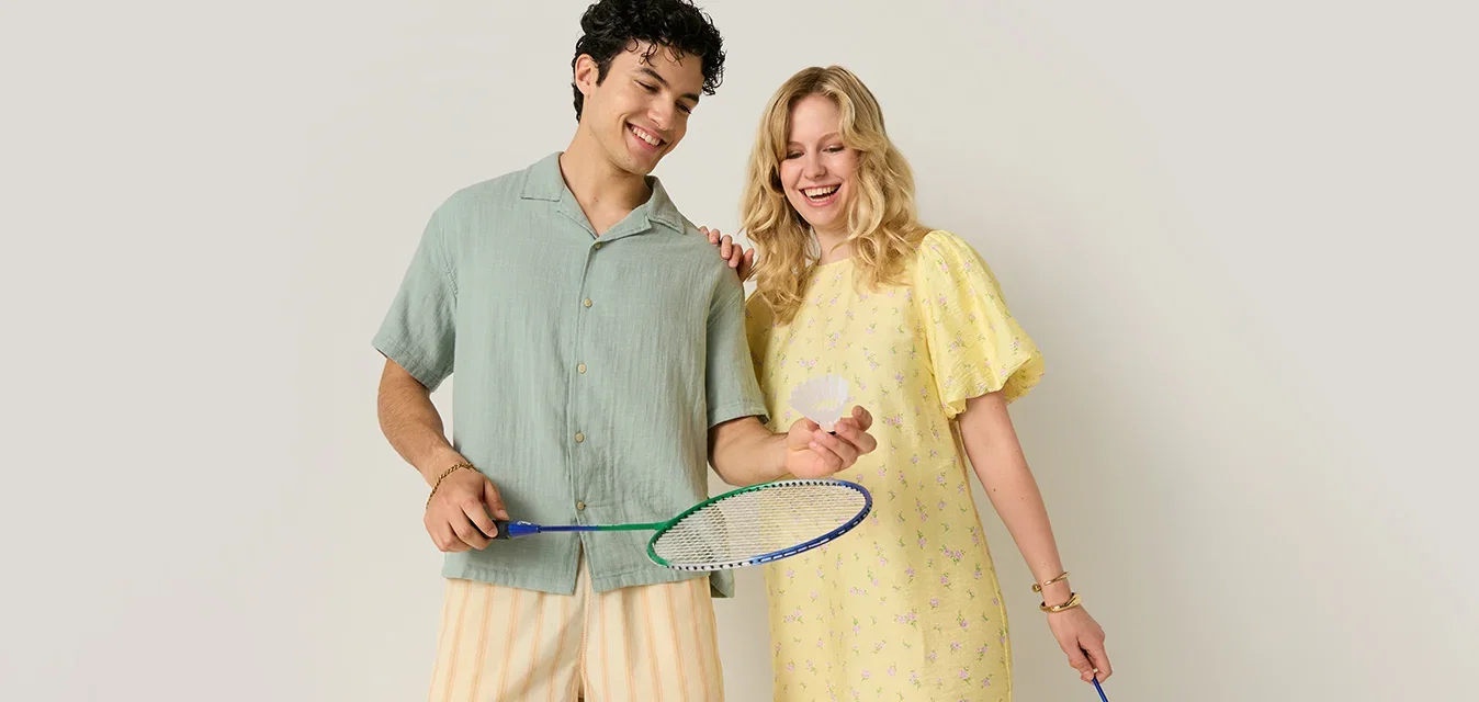 Giovane uomo e donna sorridenti mentre tengono in mano racchette da badminton, in piedi fianco a fianco davanti a uno sfondo uniforme.