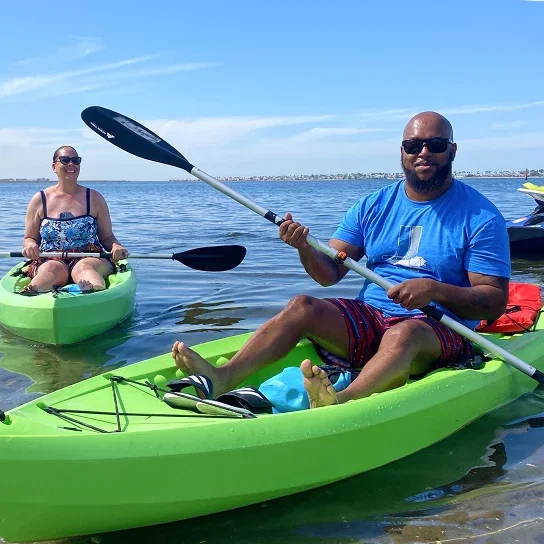 Two people paddling a green kayak on calm water.