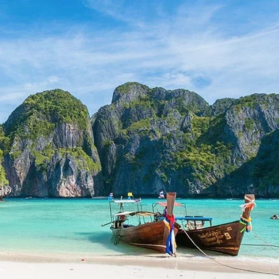 A traditional longtail boat on turquoise water beside limestone cliffs.