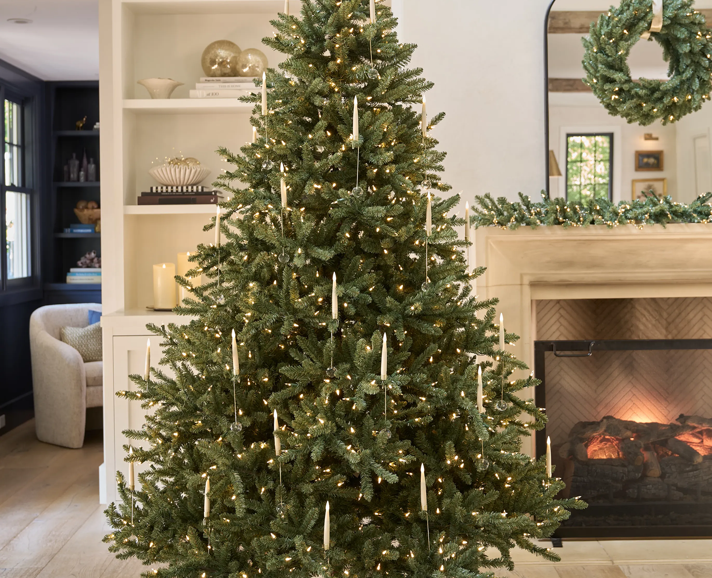 Pre-lit Christmas tree with candle-style lights in a cozy living room with a fireplace and matching wreath and garland.