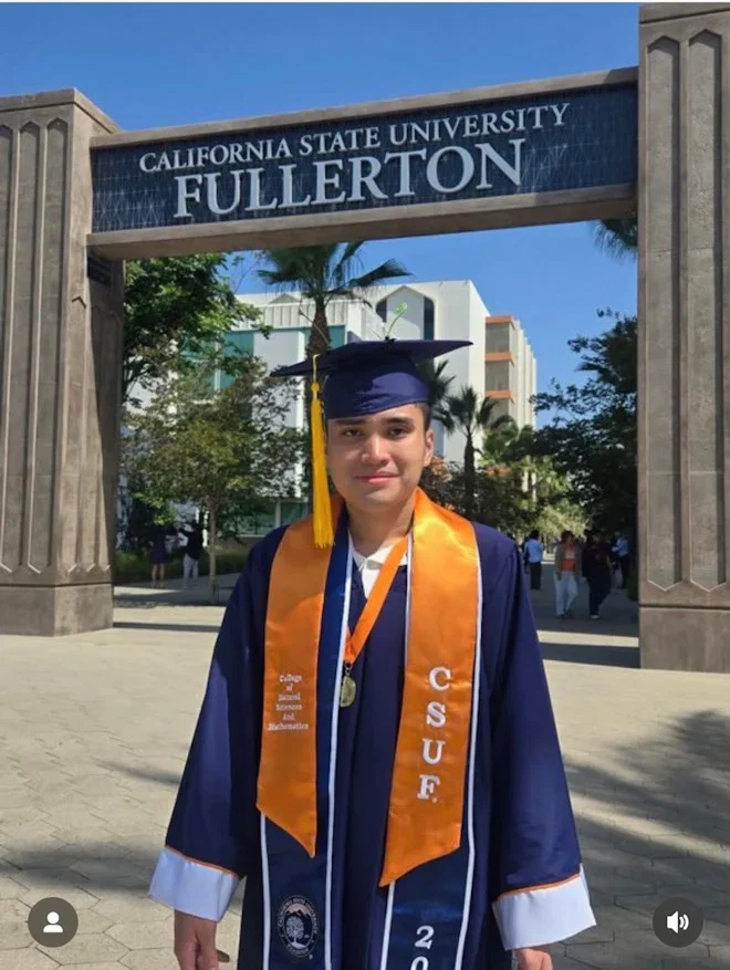 Jake wearing is graduation cap and gown while standing beneath Cal State Fullerton sign