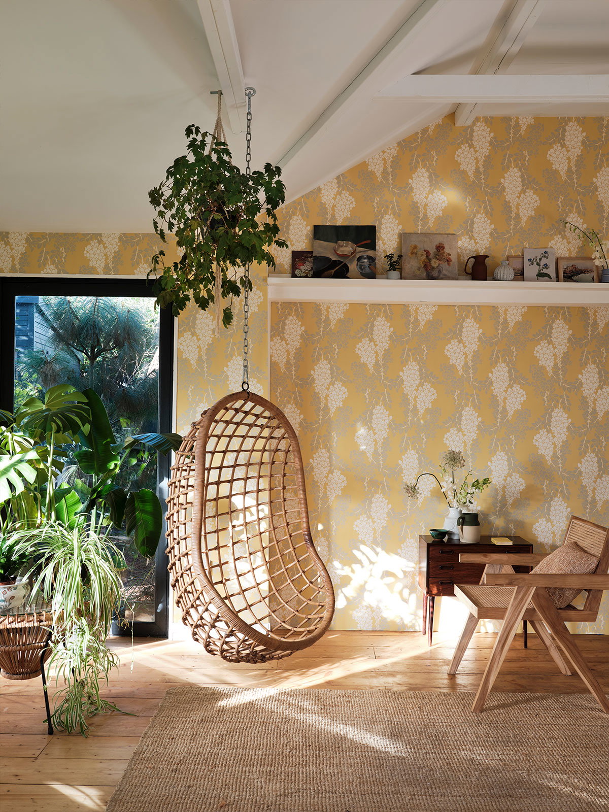 Bright room with yellow floral wallpaper, hanging wicker chair, and indoor plants.