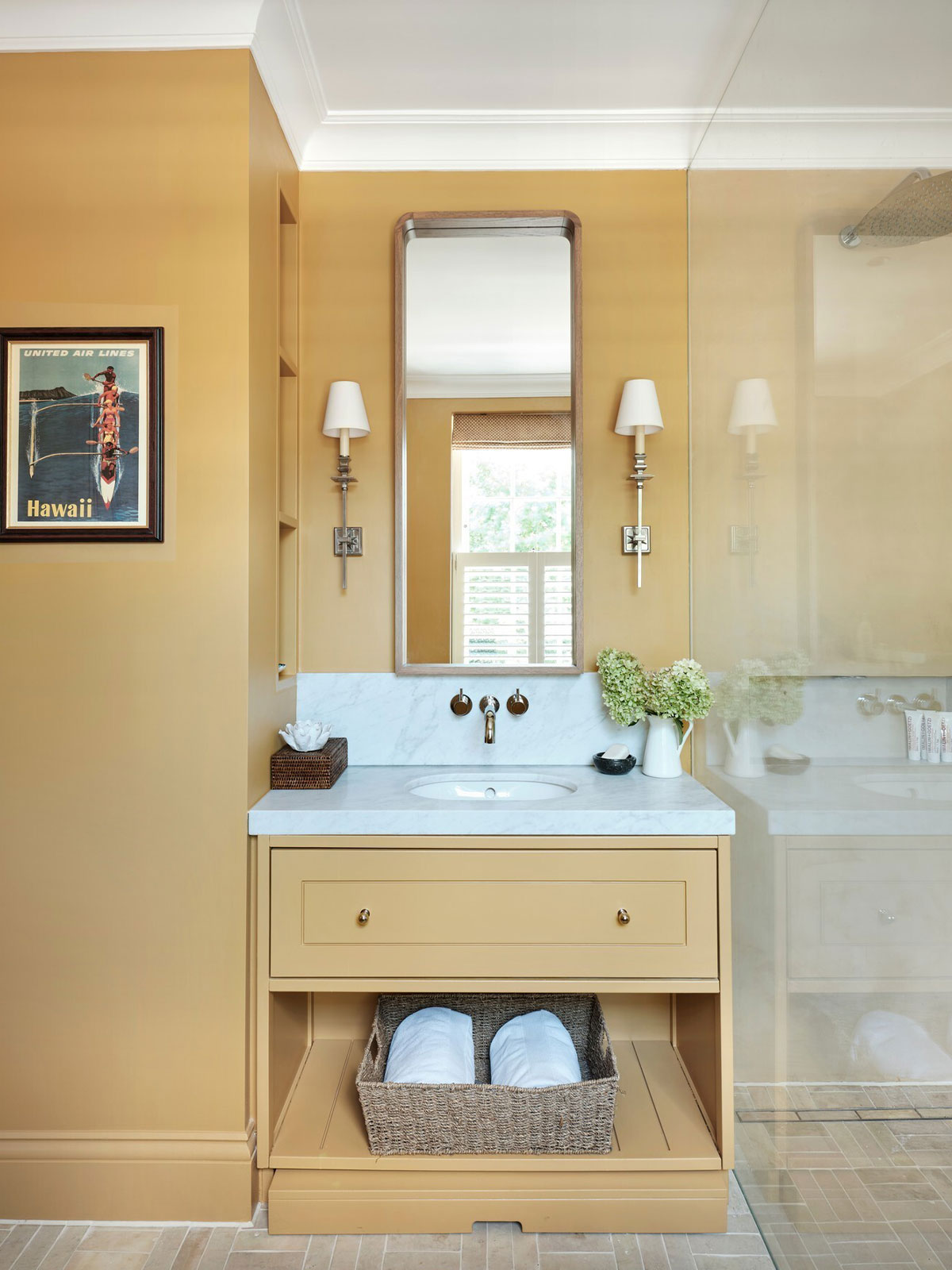 Mustard-toned bathroom with marble sink, brass fittings, and a framed Hawaii poster.
