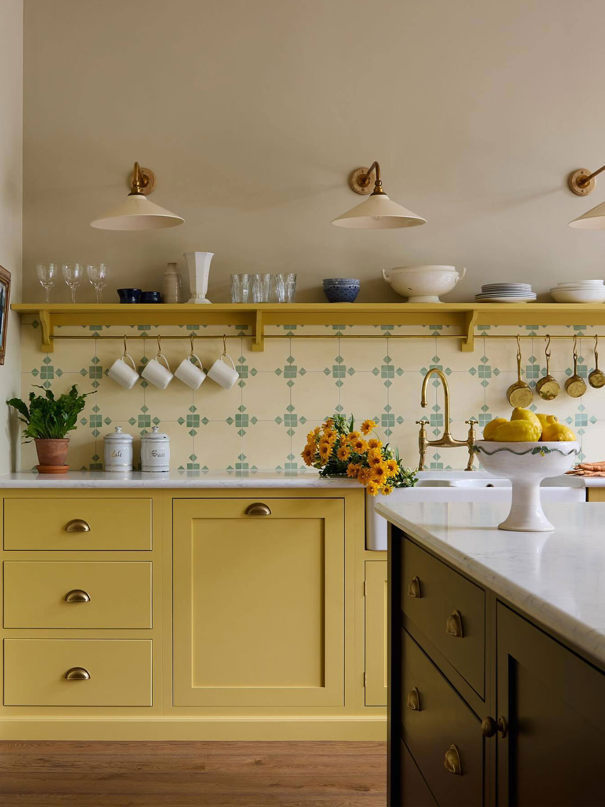 Warm yellow kitchen with brass handles, patterned tiles, and a vase of yellow flowers.