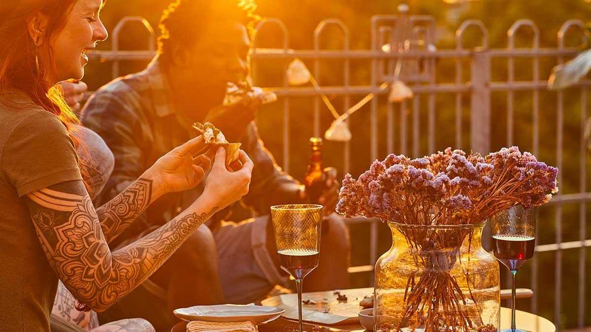 A man and woman enjoying eating pizza in the garden at sunset.