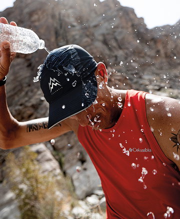 Man pouring water over his cap.