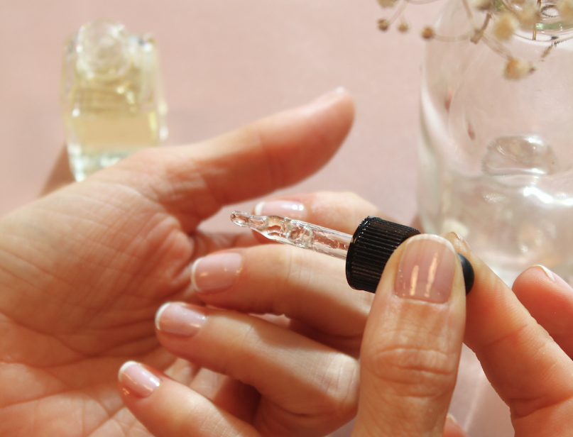 Hand applying cuticle oil with a dropper to neatly manicured nails.