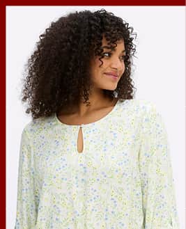 Ein Model trägt eine ecru-eisblau-gemusterte Tunika mit Blumenprint und Taillen-Gummizug . Darunter der Text: Blusen & Tuniken.