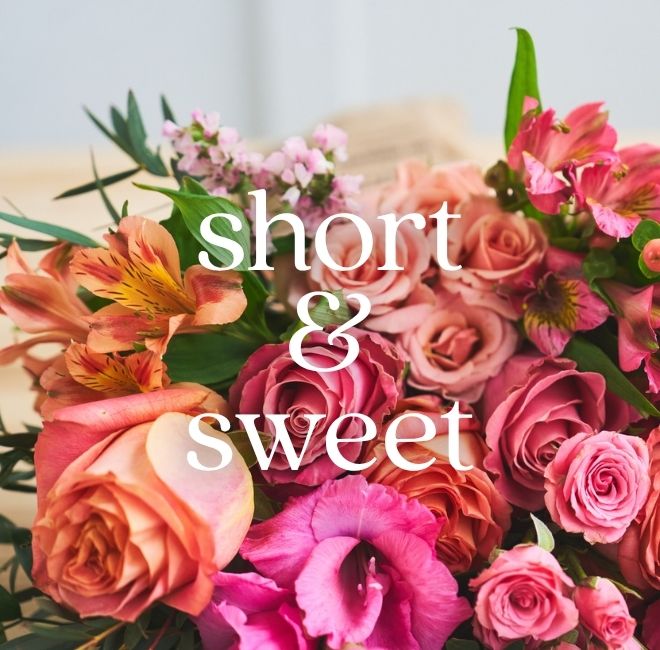 A close-up of a vibrant bouquet in coral, hot pink, and orange—roses, alstroemeria, and lisianthus; white script text over the image reads 