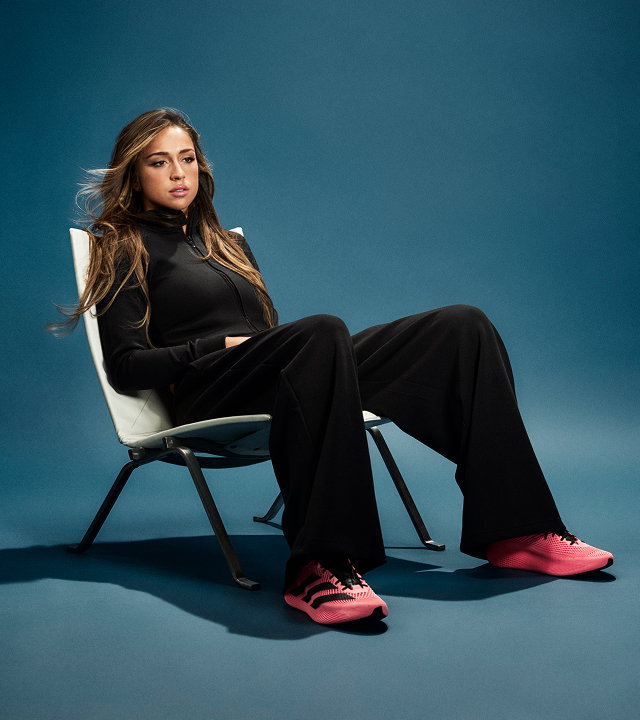 Tate McRae sitting in a chair wearing pink climacool shoes